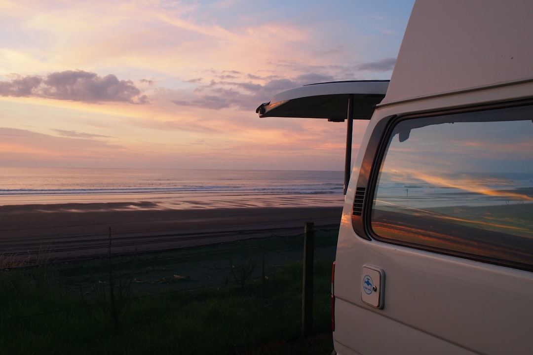 white-vehicle-parked-near-ocean-during-golden-hour-0epkj3jitao